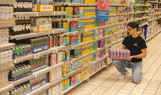 Férfi italokat pakol polcra szupermarketben.